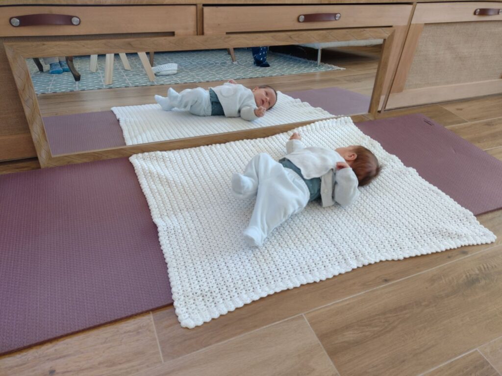 Baba a Montessori mozgásszőnyegen, vízszintes tükör előtt fekve, mint a Montessori baba szoba része