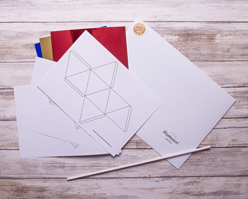 Lapképen elrendezett DIY Montessori Oktaéder forgó elemei: színes papírelemek, zsinórok és fa pálca.