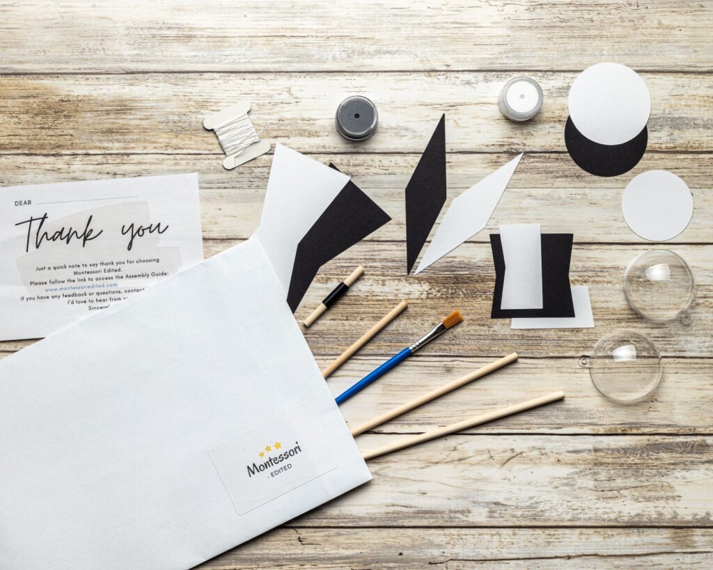 Vista cenital del kit DIY del móvil Montessori Munari con varillas, formas en blanco y negro y la esfera transparente.