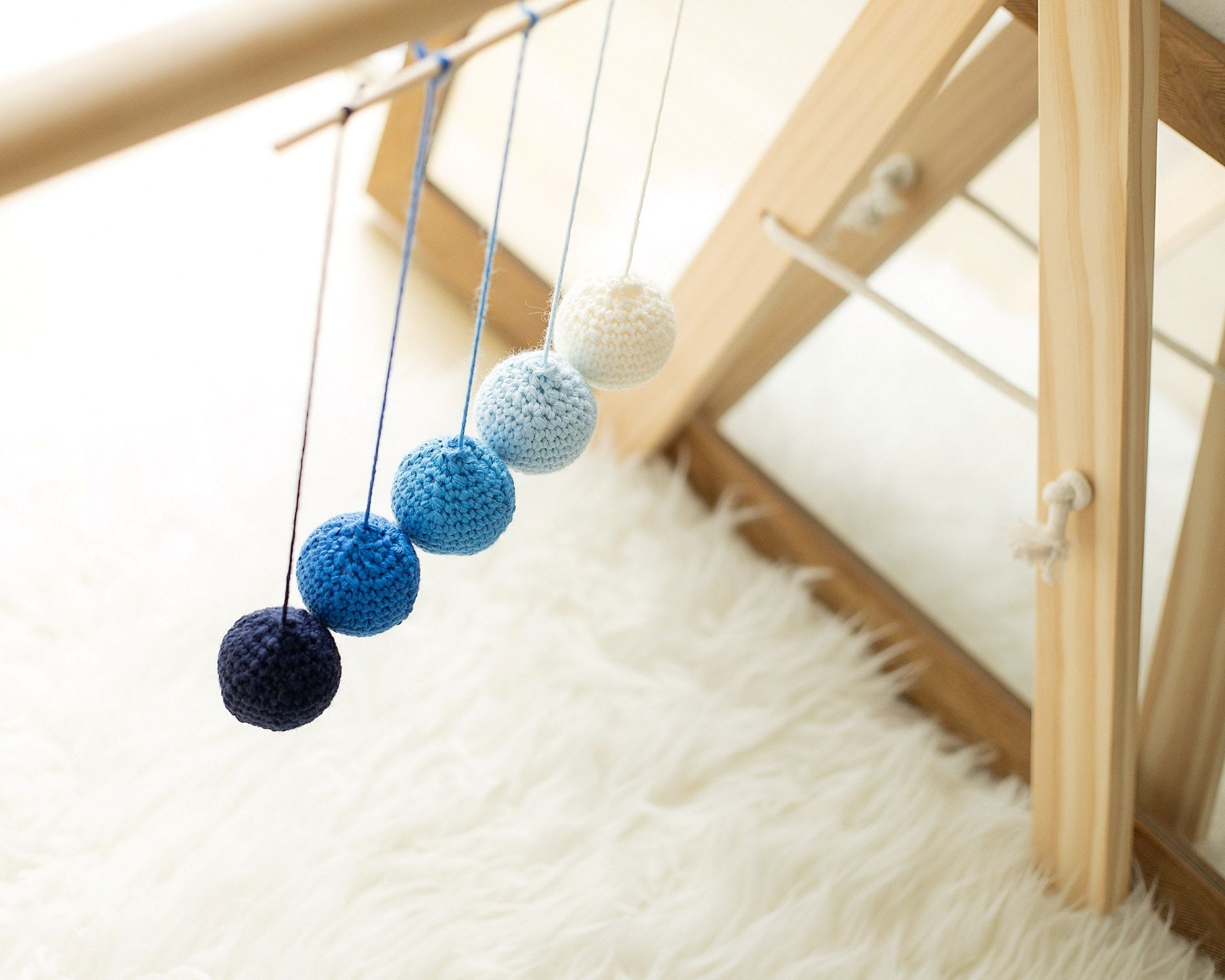 Montessori Gobbi Mobile in soft blue gradient tones hanging from a wooden baby gym beside a mirror – Montessori sensory activity supporting newborn vision and depth perception.