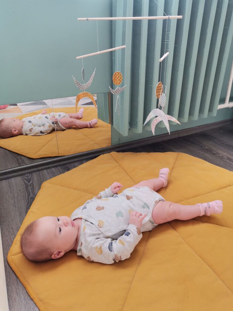 Baby observing a Dancers mobile as vision and movement begin to connect - vision development. Montessori visual mobile hung at a safe distance above the baby’s chest.