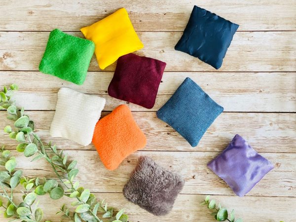 9 of the Sensory Bean Bags thown on a wooden surface with some greenery in one corner.