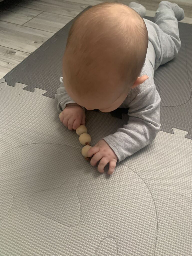 bebé explorando cuentas de agarre Montessori sobre una alfombra de movimiento