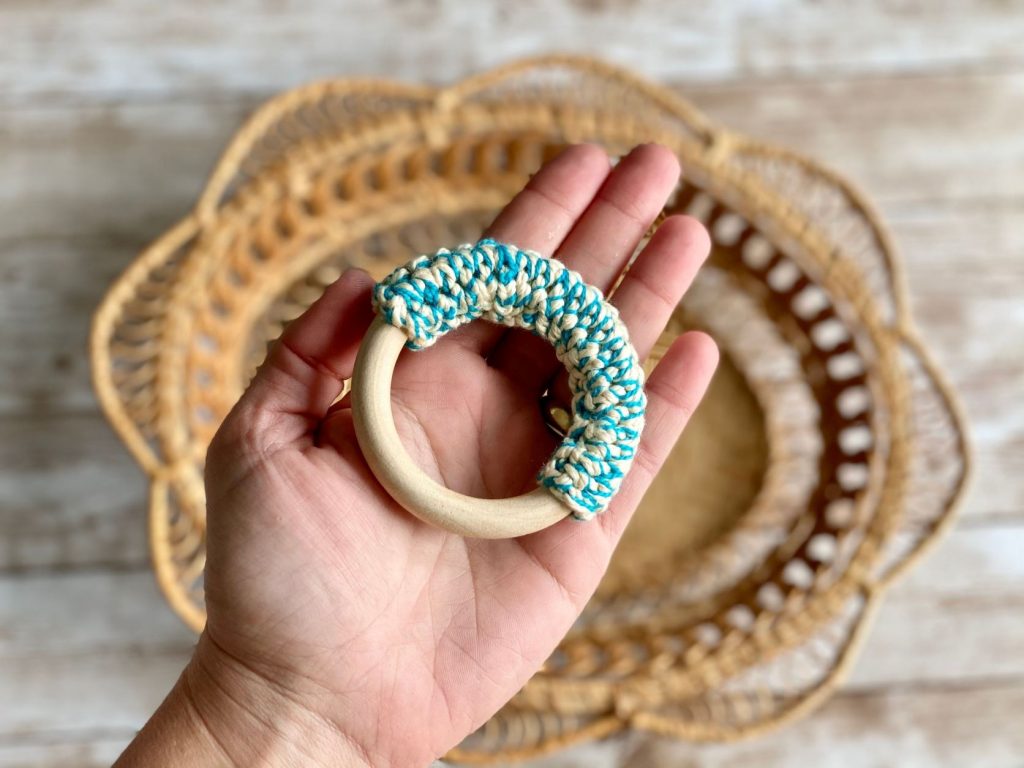A crochet teething ring in hand for scale
