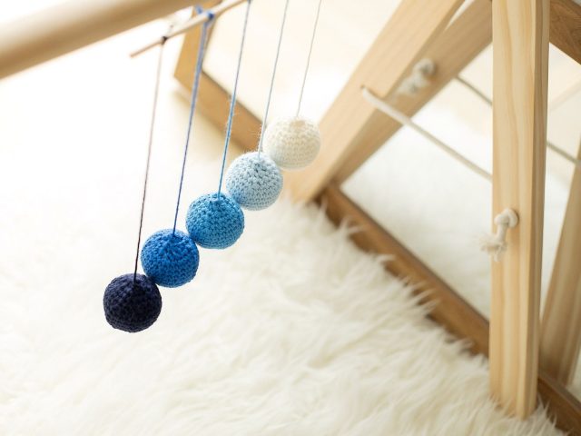 Montessori Gobbi Mobile in soft blue gradient tones hanging from a wooden baby gym beside a mirror – Montessori sensory activity supporting newborn vision and depth perception.