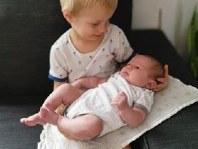 Montessori baby routine, a little boy is sitting on a sofa, holding his baby brother